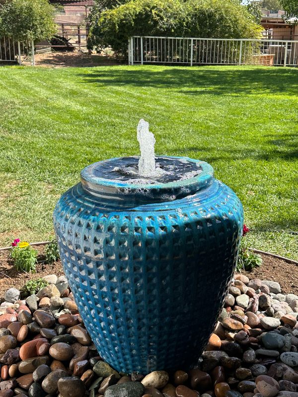 Blue glazed ceramic urn fountain set in river rock beside a lawn
