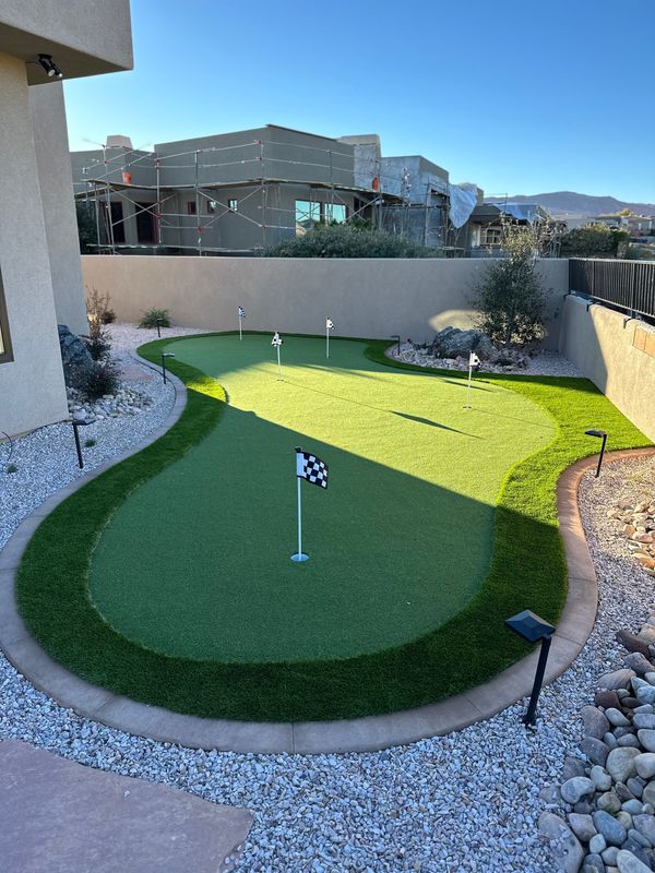 Multi-hole putting green with flags, stained concrete curbing, rock, and landscape lights between stucco walls